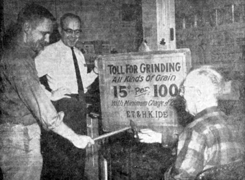 Fred Johnson, employee at E.T. and H.K. Ide Inc., for 41 years, explains use of hammer for smoothing “buhr” which were used about 1900 for grinding grain. Sign held by Richard Ide, owner of the business, is about 60 years old. John Ide, left, son of Richard, is sixth generation of family to become member of the firm.